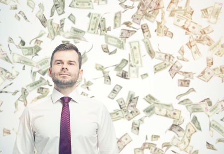 Confident businessman standing under dollar bill rain on sunny day. Concept of successful business. Mockup. Toned imageの写真素材