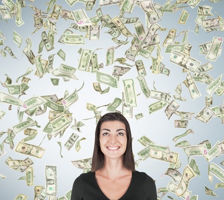 Smiling girl standing under dollar rain against light gray wall background. Concept of sudden money acquisitionの写真素材