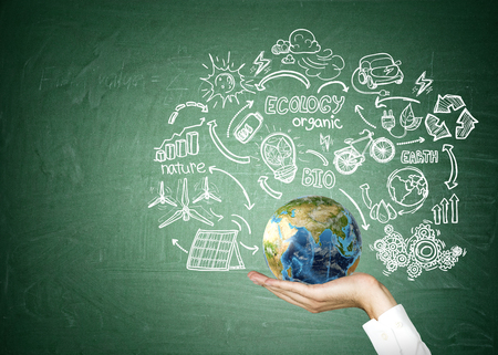 Close up of man's hand holding globe surrounded by sketches of renewable energy sources. Concept of being responsible. Mock up. Elements of this image furnished by NASAの写真素材