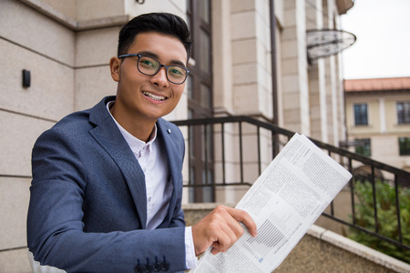 Smiling Asian businessman holding newspaper and smiling to the viewer. Concept of confident manの写真素材
