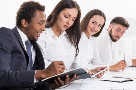 Cheerful African American businessman is making notes while sitting in his office and looking at his colleague's tablet computer. Concept of teamworkの写真素材