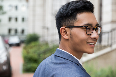 Close up of successful Asian businessman wearing glasses at the street of his hometown. Concept of prosperity and personal growthの写真素材
