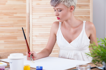 Serious woman painter is creating her masterpiece in office with wooden screen and a potted plant. Concept of designの写真素材