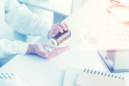 Doctor sitting at table and putting several pills on palm, only hands seen. Concept of medical help. Toned imageの写真素材