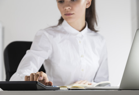 Close up of counting office employee. She is sitting in white office and using her gadgets and office electronics. Concept of a brave new worldの写真素材