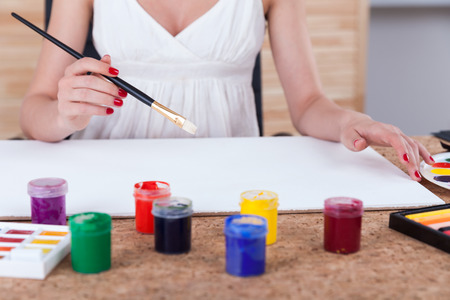 Close up of woman painter's hands holding a brush and starting to paint on large sheet of paper. Concept of creative workの写真素材