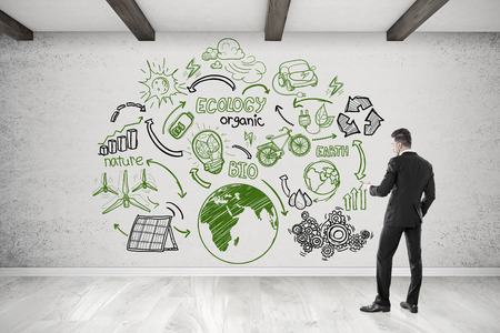 Rear view of man with cellphone looking at ecology sketch on concrete wall. Concept of green business.の写真素材