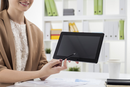 Close up of smiling woman in beige pointing at her tablet computer screen. Concept of working in the office. Mock upの写真素材