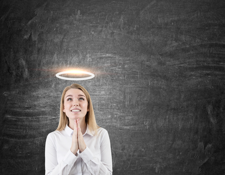 Hoping woman with a halo above her head is standing against blackboard. Concept of holiness. Mock upの写真素材