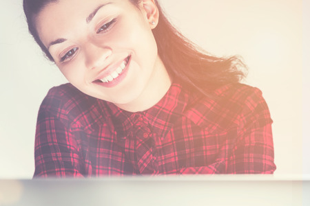 Smiling girl in red shirt is sitting near her laptop and looking at the screen. Concept of gadget use. Mock up. Toned imageの写真素材