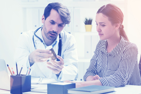 Young doctor is showing his patient bottle of pills and explaining how they work. Concept of medical care. Toned imageの写真素材
