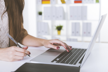 Close up of woman in white lace shirt  typing at laptop keyboard in office. Concept of computers in our lives.の写真素材