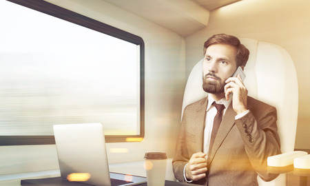 Bearded businessman is travelling in first class train and using his smartphone. Concept of business trip. 3d rendering. Mock up. Toned image.の写真素材