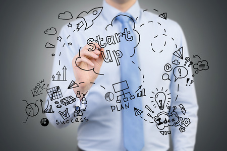Close up businessman in blue shirt who is drawing project launching sketch on glassboard while standing against black background.の写真素材
