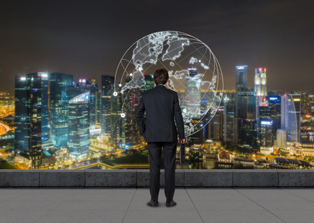 Rear view of businessman standing against night  large city panorama and enjoying the view. Concept of CEOの写真素材