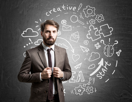 Businessman in brown suit is standing near round startup sketch drawn on chalkboard. Concept of small business founderの写真素材