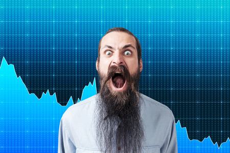 Shouting man with long beard is standing against blue background with graphs on it. Concept of stock market crisis.の写真素材