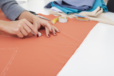 Close up of beautiful woman's hands drawing a pattern on orange tissue. Measuring tape and sewing...