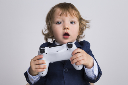 Surprised little boy holding a game controller and looking to the camera. Concept of gaming
