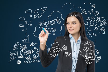 Close up of black haired woman drawing startup sketch on glassboard. Blue wall in the backgroundの写真素材