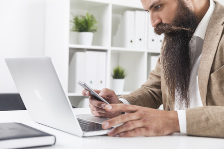 Side view of businessman with long beard and magnificent moustache looking at his mobile phone screenの写真素材