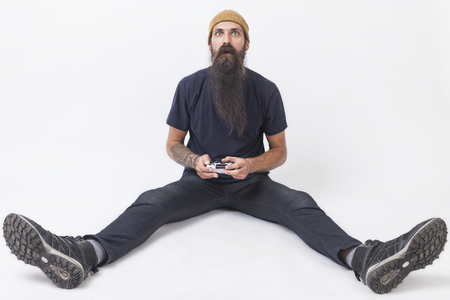 Hipster guy with long beard wearing a beanie is holding a video game controller and looking baffled...