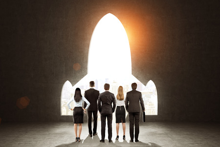 Rear view of a business team standing near black wall with a plane shaped opening in it. Concept of project launching. Toned imageの写真素材