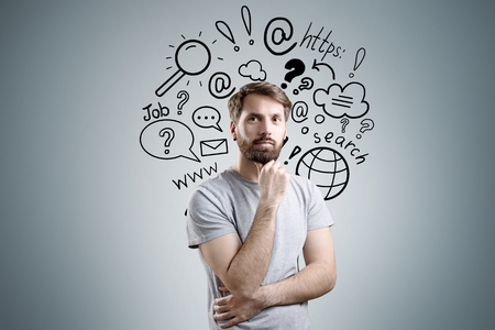 Portrait of bearded man in a T-shirt standing near gray wall with internet search sketches on itの写真素材