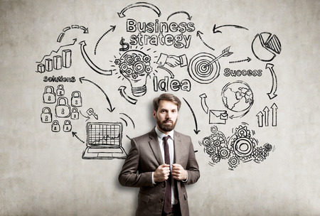 Bearded businessman is standing near a concrete wall with business strategy sketch drawn on itの写真素材