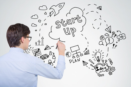 Side view of young businessman in blue shirt drawing project sketch on light gray wall. Concept of planning in businessの写真素材