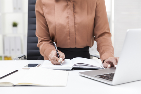 Close up of woman in brown blouse; taking notes with the second. Concept of secretary's jobの写真素材
