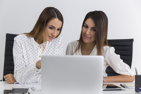 Two businesswomen are sitting at one laptop and looking at its screen. One is showing something to her colleagueの写真素材