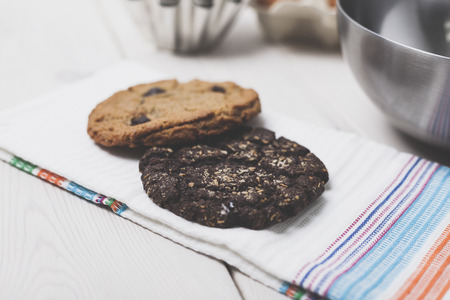 Two homemade cookies lying on a towel. Metal bowl is standing on a wooden table. Concept of eating healthyの写真素材