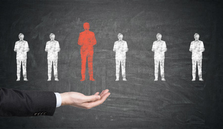 Close up of a businessman's hand holding a red figure drawn on a blackboard. There are smaller white figures on it too. Concept of HRの写真素材