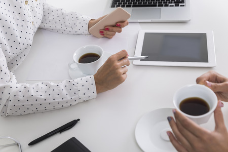 Close up of two pairs of women's hands. One is holding a smartphone and a pen. The second is holding...