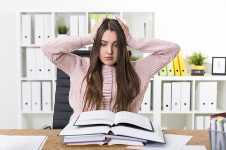 Portrait of a woman wearing a pink sweater and being overwhelmed with the number of books she is supposed to read.の写真素材