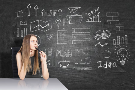 Woman with blond hair is sitting at her table in class. There is a startup sketch on the blackboardの写真素材