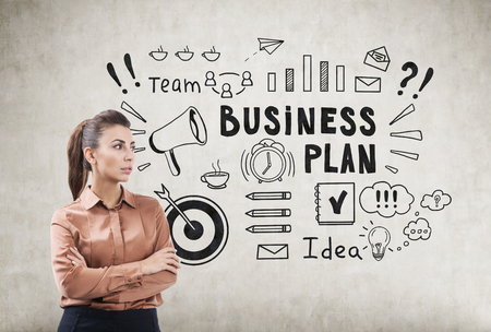Woman in brown blouse is standing with her arms crossed near a business plan sketch on a concrete wall.の写真素材