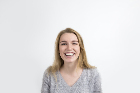 Positive blond woman in a gray sweater is smiling broadly and looking to the camera. Concept of...