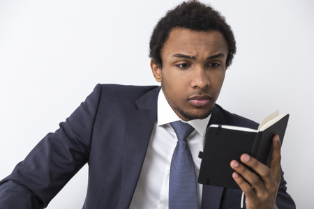 Close up of an African American man reading a small black notebook and looking serious. Concept of getting ready for a board meeting.の写真素材