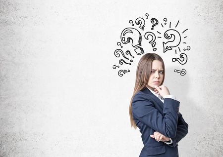 Portrait of a frowning woman in a business suit. She is plotting a suspicious action near a concrete wall with question marks on it. Mock upの写真素材