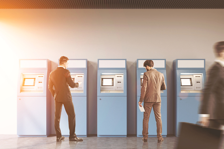 Hallway of an office or a bank. A man is rushing by. Two businessmen are standing near ATM machines. There is a cityscape on the foreground. Toned image.の写真素材