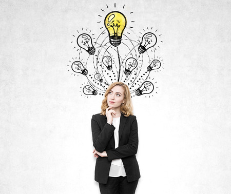 Portrait of a pensive redhead woman with a her hand near her face standing near a concrete wall with a yellow light bulb sketch.の写真素材