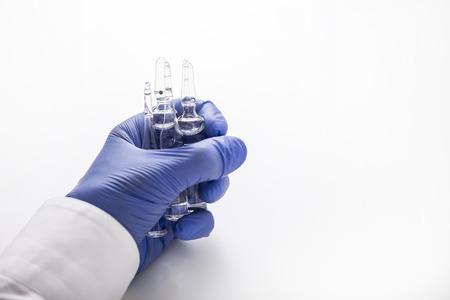 Close up of a man's hand in a blue rubber glove holding several vials with transparent liquid. Concept of a farmacist's work. Mock upの写真素材
