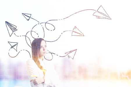 Portrait of a woman with braided hair standing in a city and thinking. There are paper planes flying around her. Blurred. Concept of daydreaming. Toned image. Mock up.の写真素材