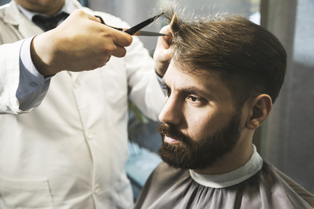Side view of barber’s hands cutting a serious businessman’s brown hair. Concept of looks...