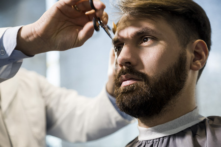 Close up of a bearded businessman having his hair cut in a barber shop. Concept of being well groomedの写真素材