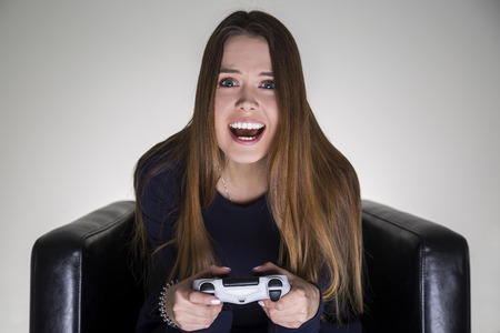 Portrait of a happy teenage girl sitting in a leather armchair and holding a video game controller.の写真素材