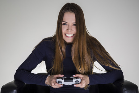 Portrait of a happy determined girl sitting in a leather armchair and holding a video game controller.の写真素材