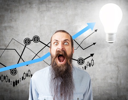 Screaming man with a long beard is standing near a concrete wall with black and blue graphs on it and a light bulb in the corner.の写真素材